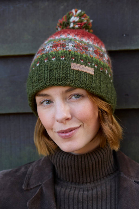 Pachamama Iona Fair Isle Bommelmütze in Moosgrün mit roten Musterdetails getragen